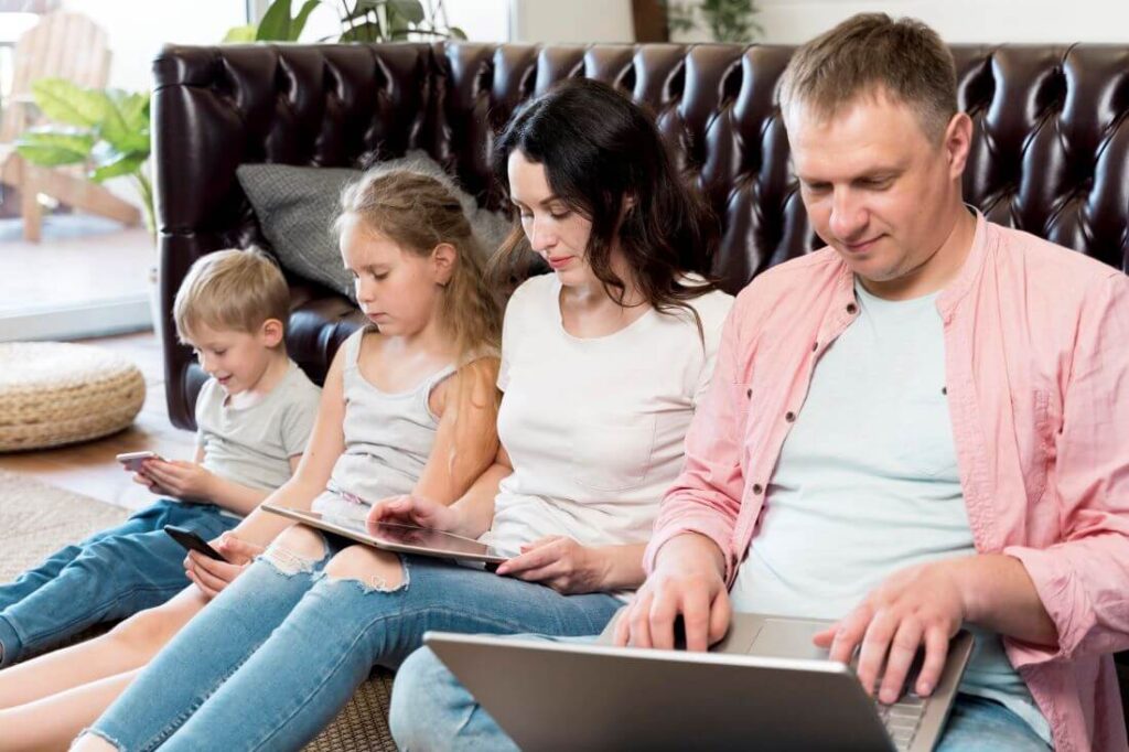 Rodzina siedząca razem, ale każdy skupiony na ekranie. Dopamina i technologia wpływają na relacje rodzinne i koncentrację.