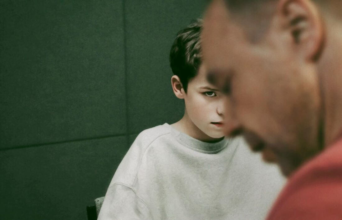 Chłopiec spoglądający z niepokojem na ojca – scena z serialu „Dojrzewanie” netflix ukazująca napięcie emocjonalne w rodzinie.